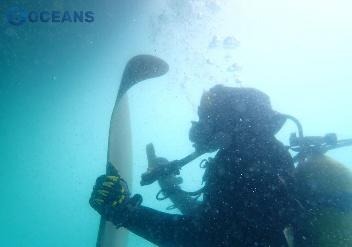 Commercial diver working on a propeller blade underwater with a hand tool