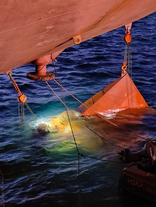Orange habitat lowered alongside a vessel's hull at night for an afloat repair