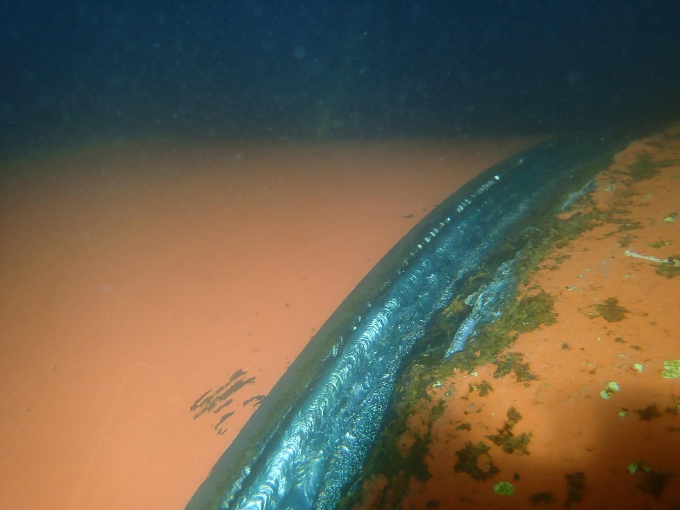 Underwater weld along the curved edge of a hull plate with marine growth alongside
