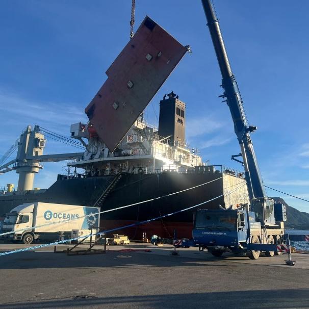 Rudder blade lifted ashore by mobile crane alongside a vessel in port